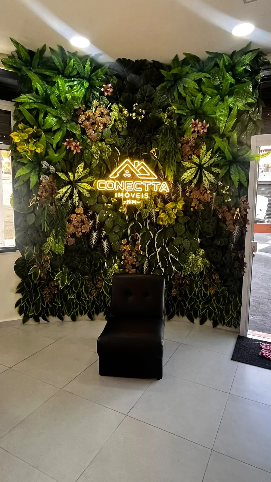 Recepção da Conectta, com parede de folhagem e a marca em neon