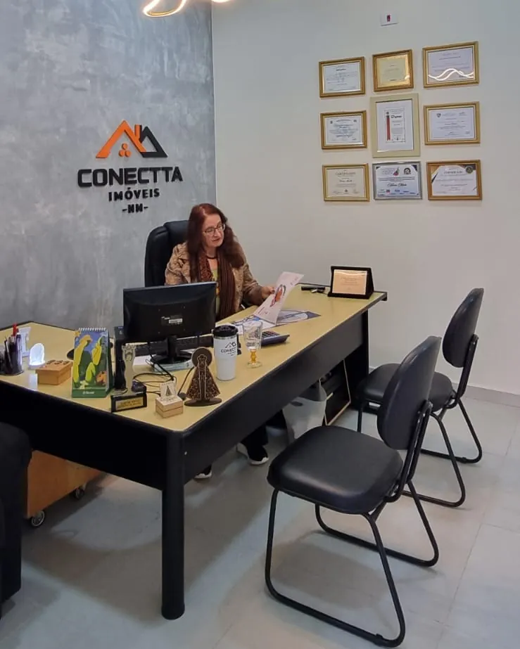 Neiva Miotto atendendo na mesa do escritório da Conectta, com os certificados na parede
